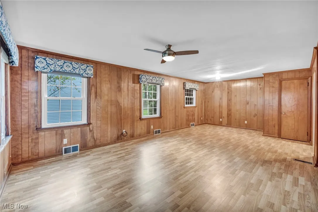 Family room with healthy amount of natural light, light wood-type flooring, wood walls, and a ceiling fan