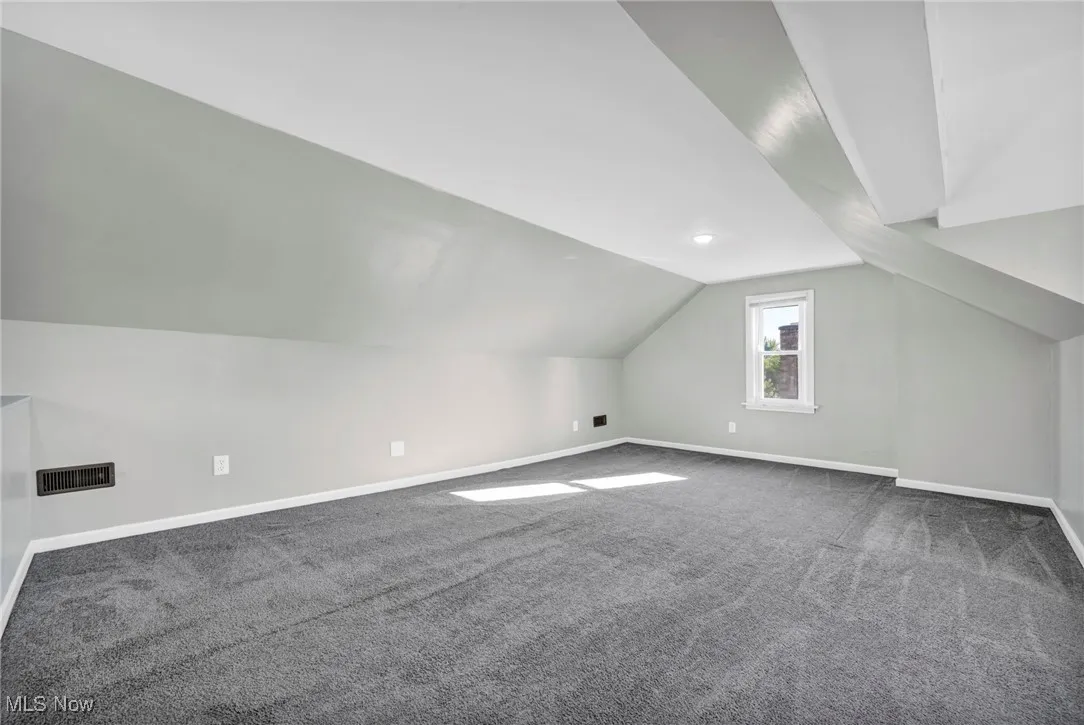 Bonus room featuring dark colored carpet and vaulted ceiling