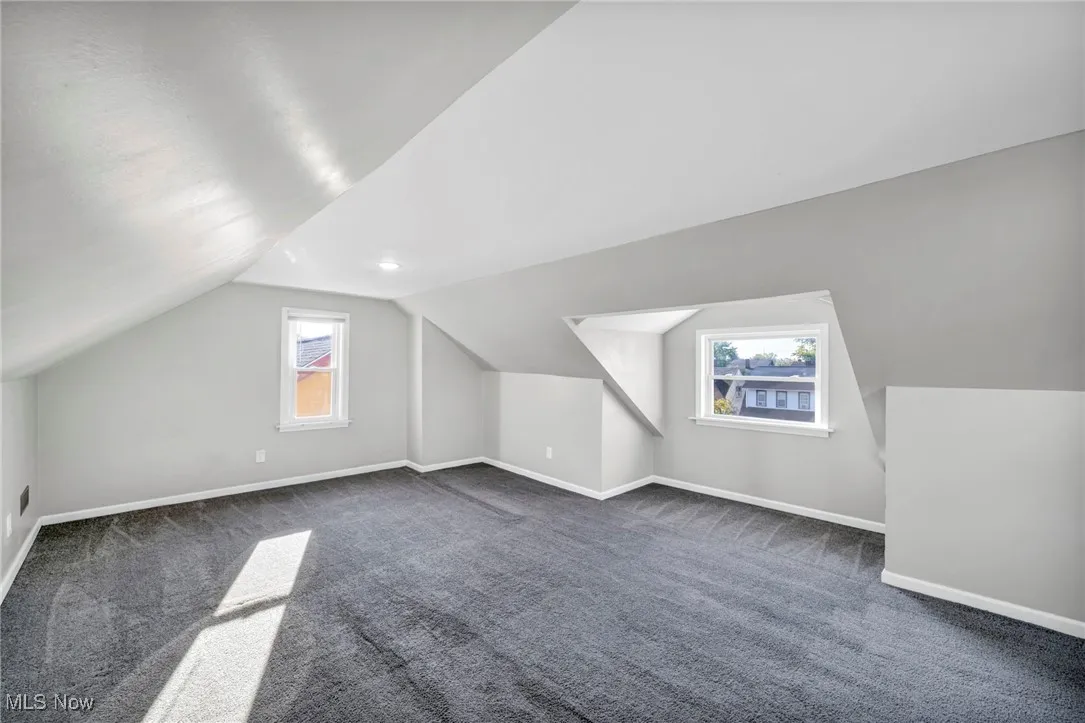 Bonus room with plenty of natural light, vaulted ceiling, and dark carpet