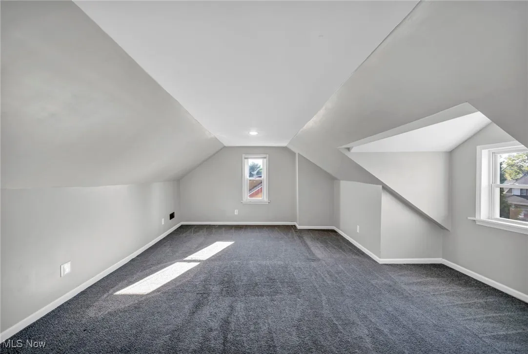Bonus room featuring dark colored carpet, plenty of natural light, and vaulted ceiling