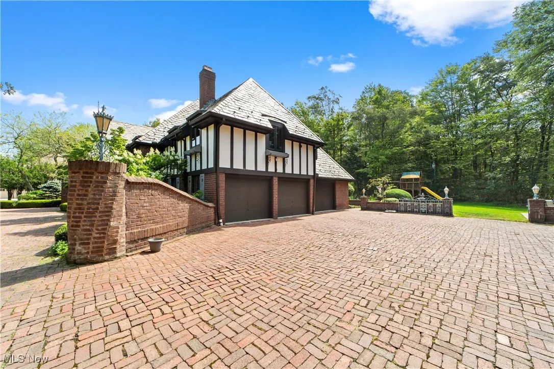 View of side of property featuring a playground, a high end roof, a chimney, a garage, and decorative driveway