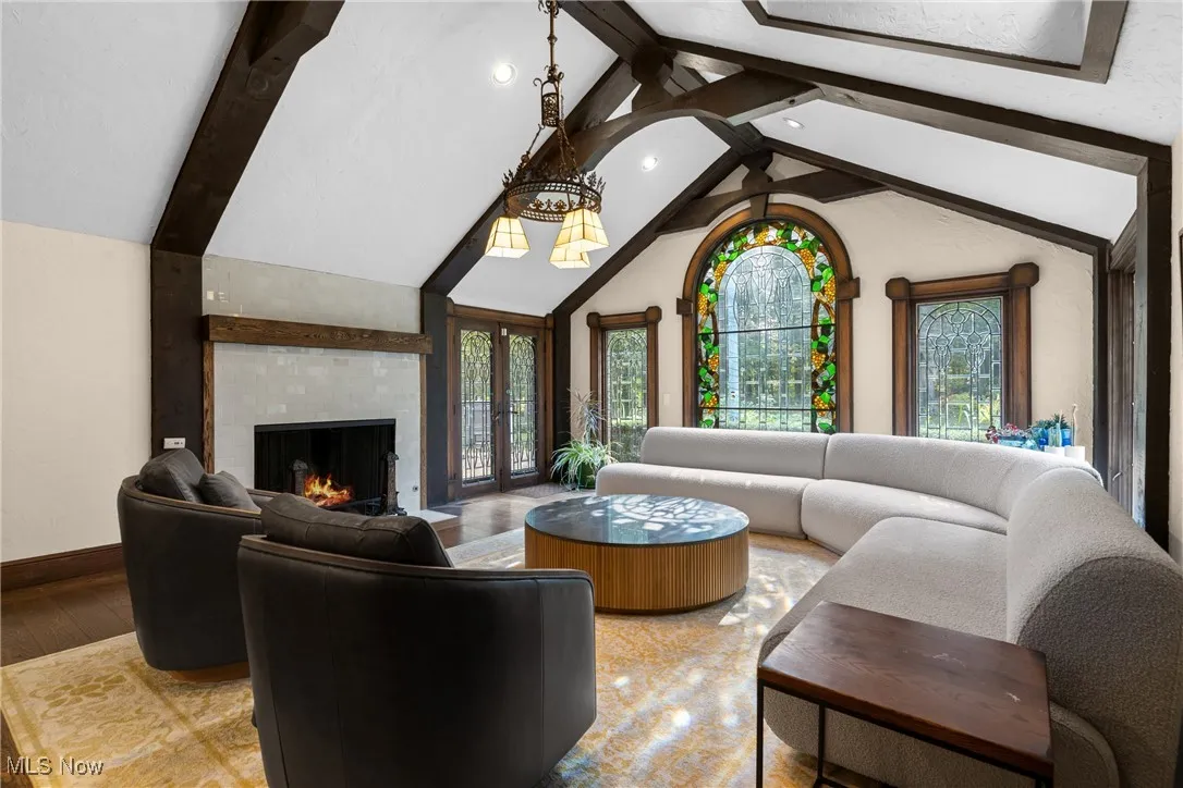 Living room with beam ceiling, a fireplace, high vaulted ceiling, wood finished floors, and french doors