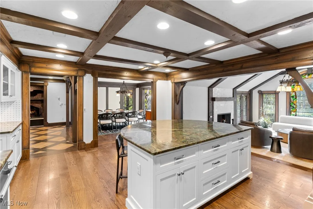 Kitchen featuring a large fireplace, a chandelier, a kitchen bar, white cabinets, and beam ceiling