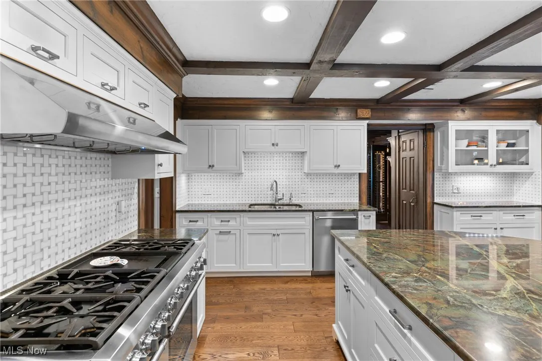 Kitchen featuring decorative backsplash, white cabinetry, appliances with stainless steel finishes, light wood finished floors, and beam ceiling