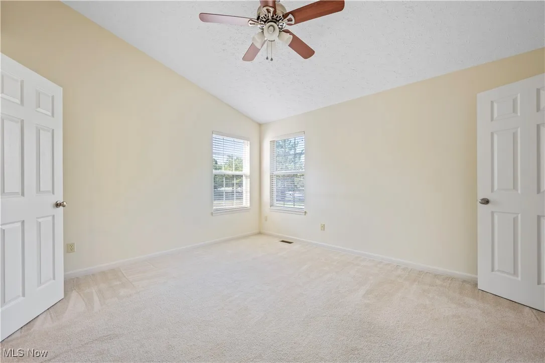 Owner's dedroom featuring vaulted ceiling, light carpet, corner windows and a ceiling fan