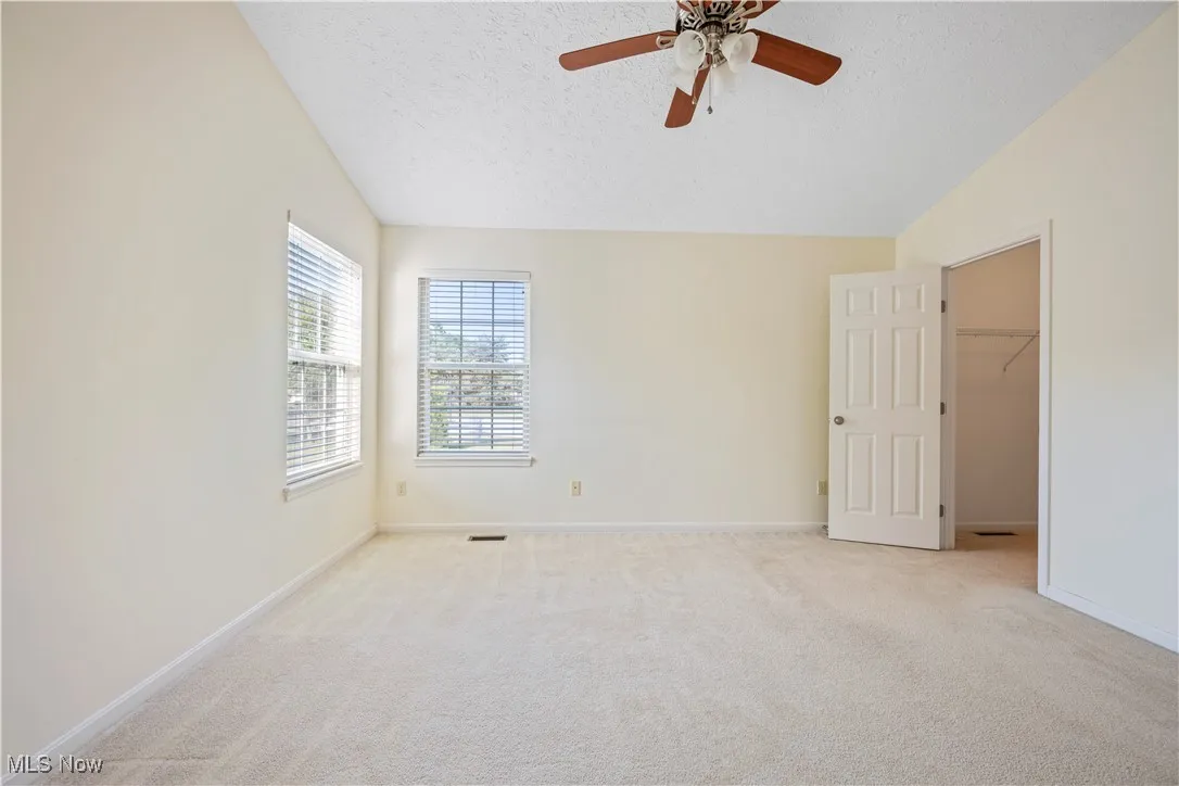Owner's bedroom with a walk in closet, lofted ceiling, light carpet, a textured ceiling, and a ceiling fan
