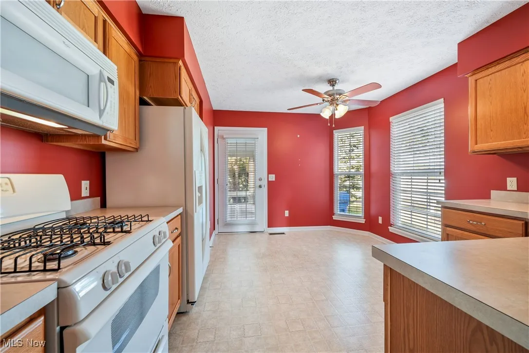Kitchen with white appliances, light countertops, ceiling fan, light floors leading to sun room