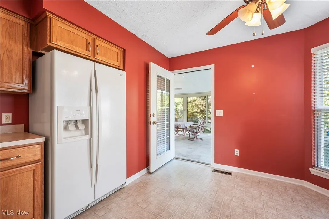 Kitchen featuring white refrigerator with ice dispenser,cabinetry, light countertops, a ceiling fan, leading to sun room