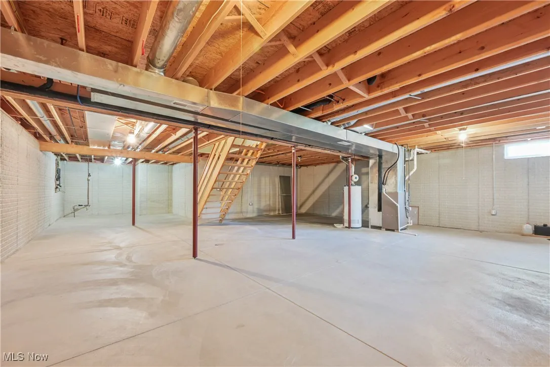 Unfinished below grade area featuring stairs, heating unit, and water heater