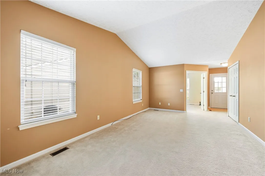 Living room with carpet flooring,vaulted ceiling and two natural light providing windows