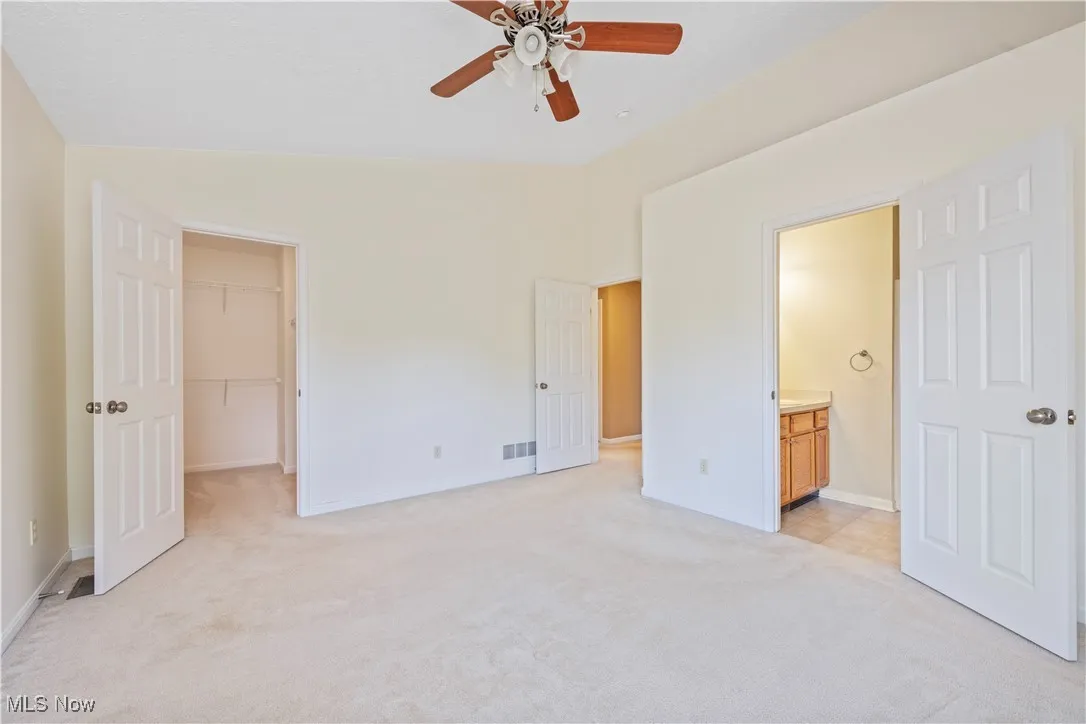 Owner's bedroom featuring light colored carpet, a walk in closet, a ceiling fan, ensuite bath, and lofted ceiling