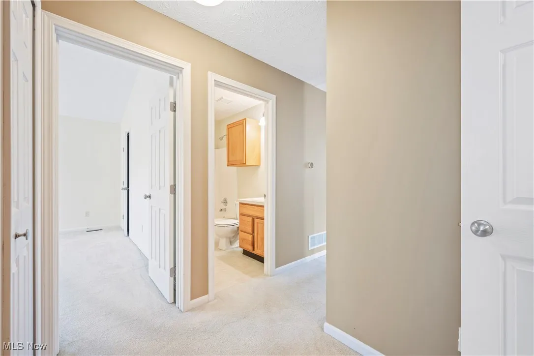 Corridor featuring light colored carpet and a textured ceiling