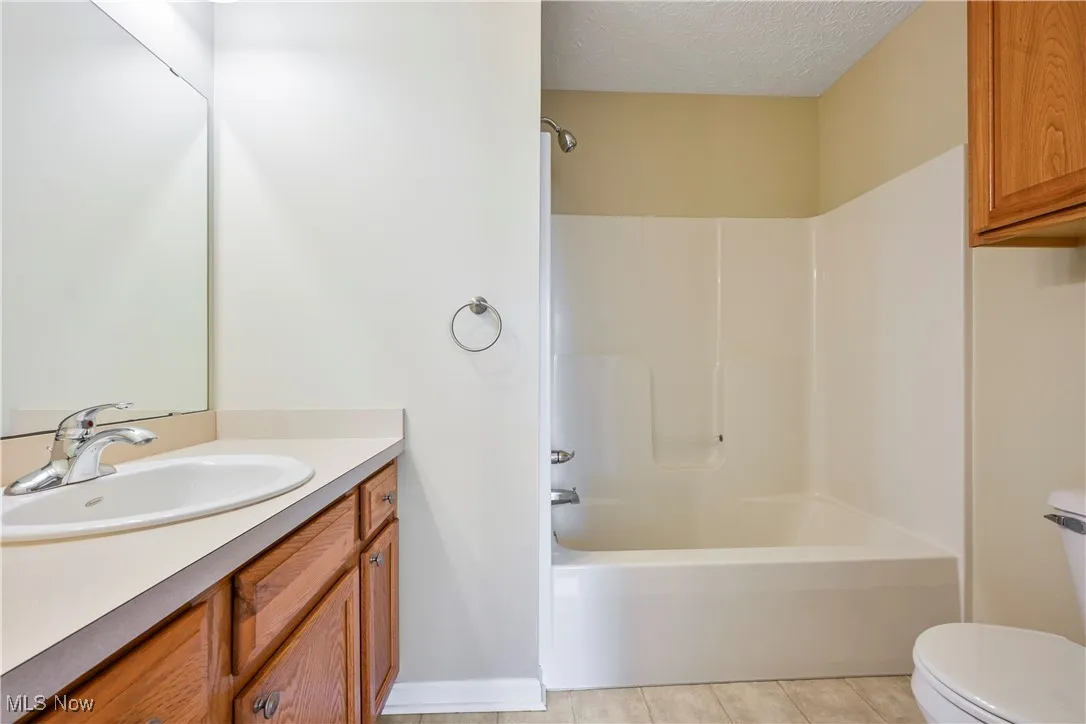 Full bath featuring a textured ceiling, washtub / shower combination, light tile patterned flooring, and vanity