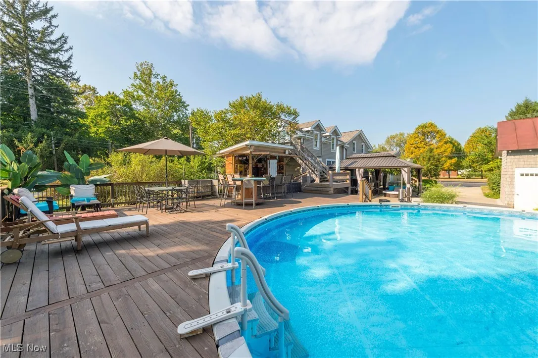 Swimming pool featuring a gazebo, a deck, outdoor dining area, and view of wooded area