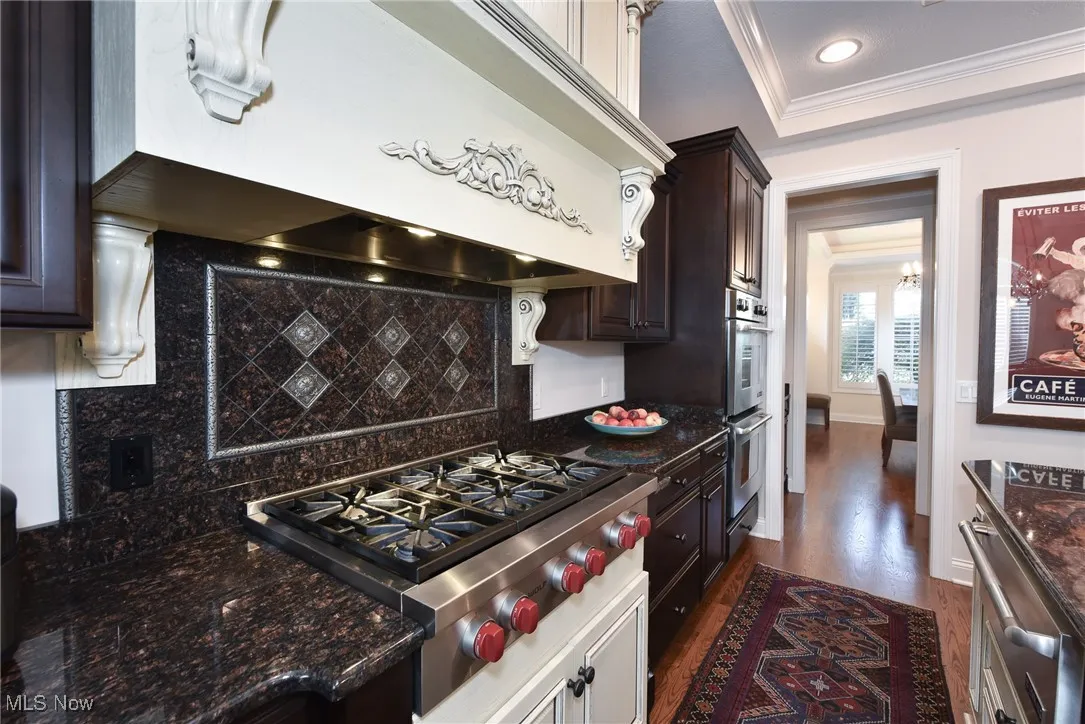 Kitchen with custom exhaust hood, dark stone countertops, appliances with stainless steel finishes, ornamental molding, and dark wood-type flooring