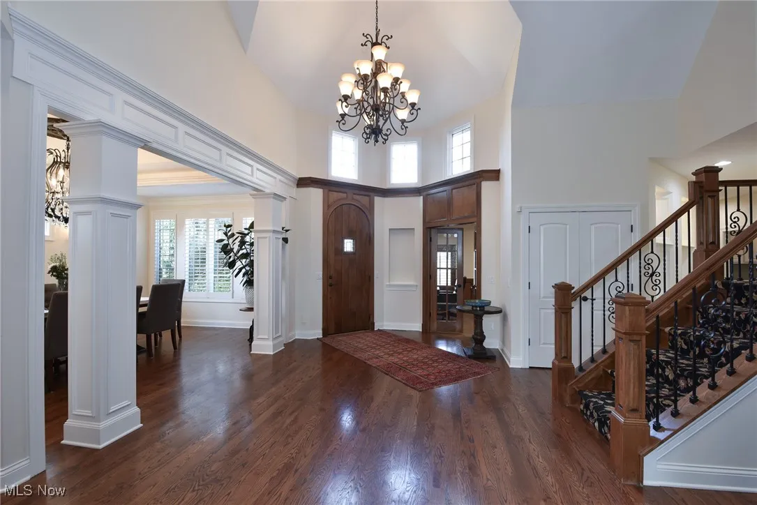 Foyer entrance with a chandelier, dark wood finished floors, a high ceiling, stairway, and decorative columns