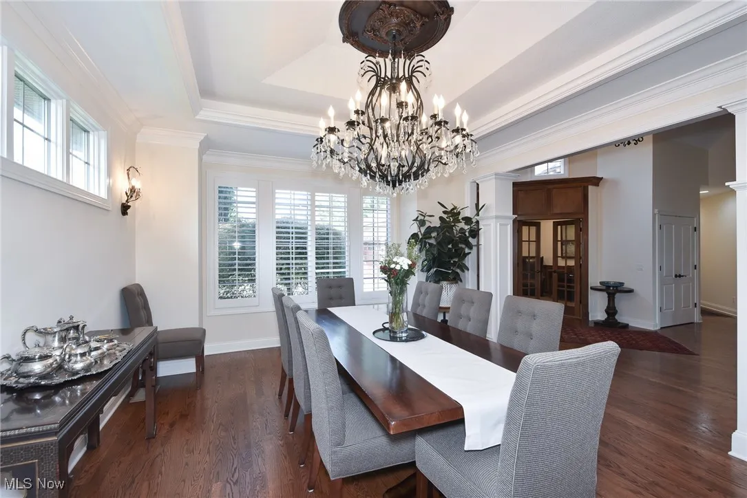 Dining area with a tray ceiling, ornamental molding, dark wood finished floors, a chandelier, and decorative columns