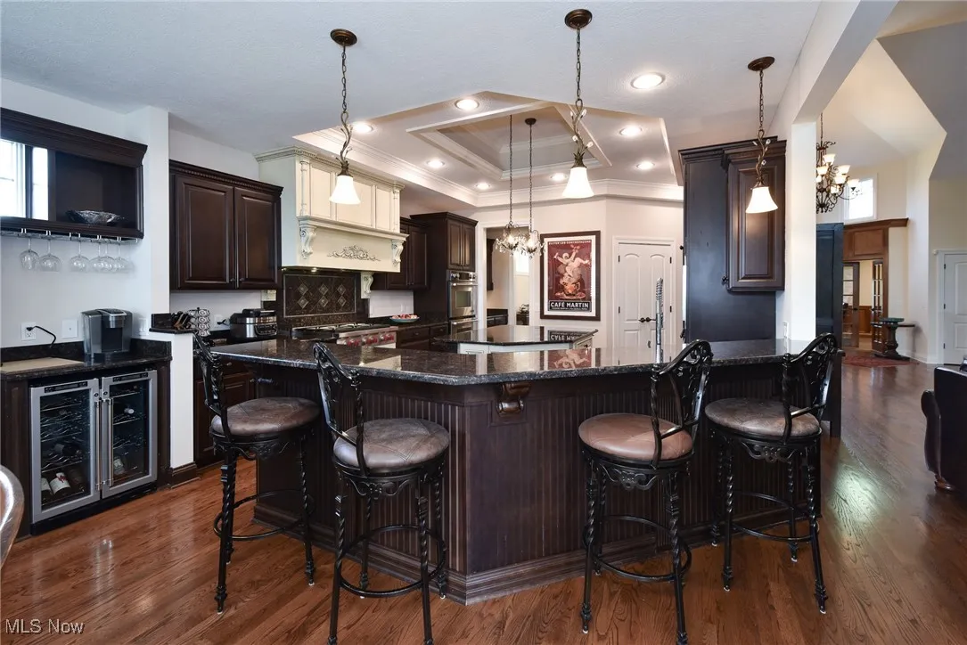 Bar area featuring dark brown cabinetry, a raised ceiling, a chandelier, dark stone countertops, and wine cooler
