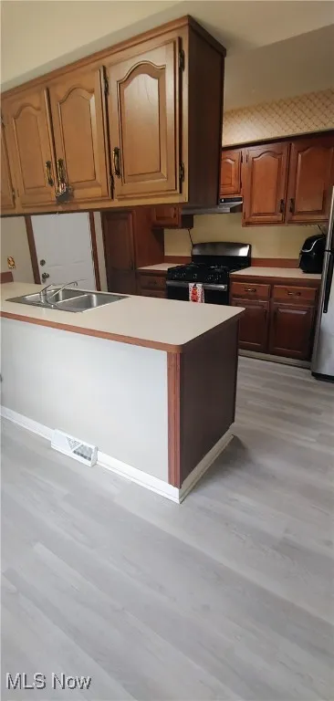 Kitchen featuring light countertops, black range with gas cooktop, light wood-style flooring, brown cabinets, and freestanding refrigerator