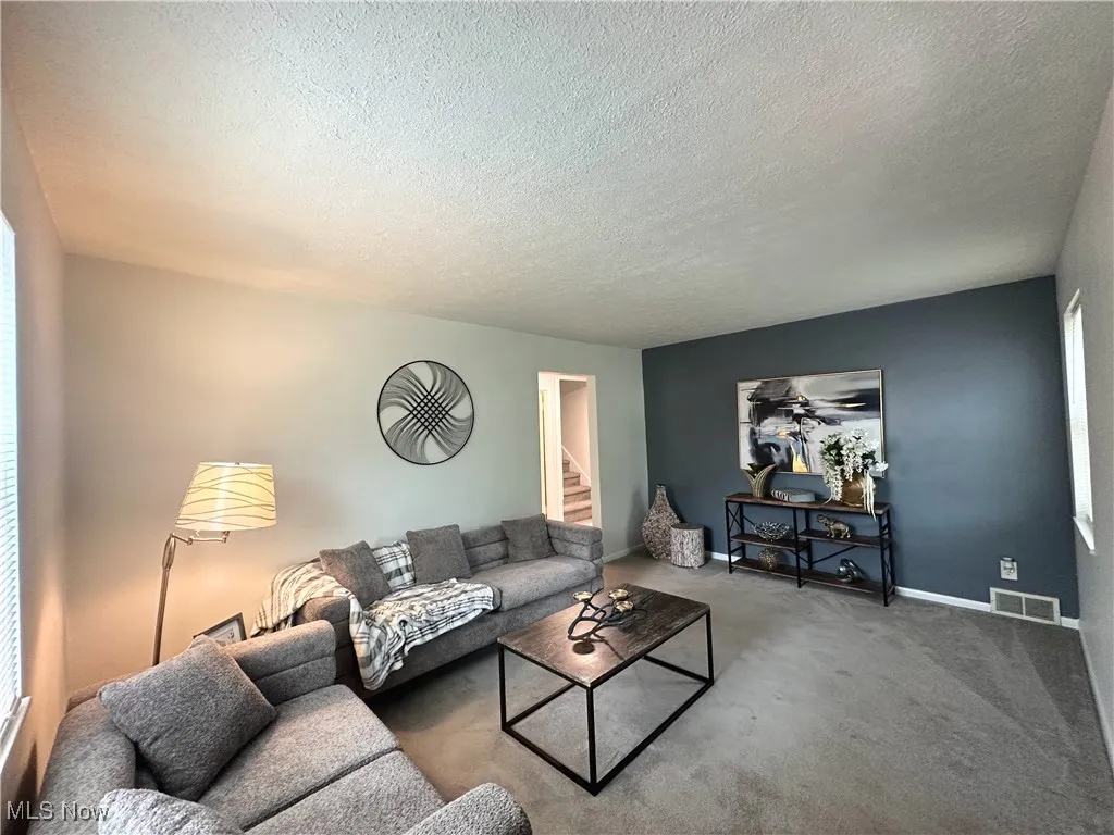 Carpeted living area with stairway, a textured ceiling, and plenty of natural light