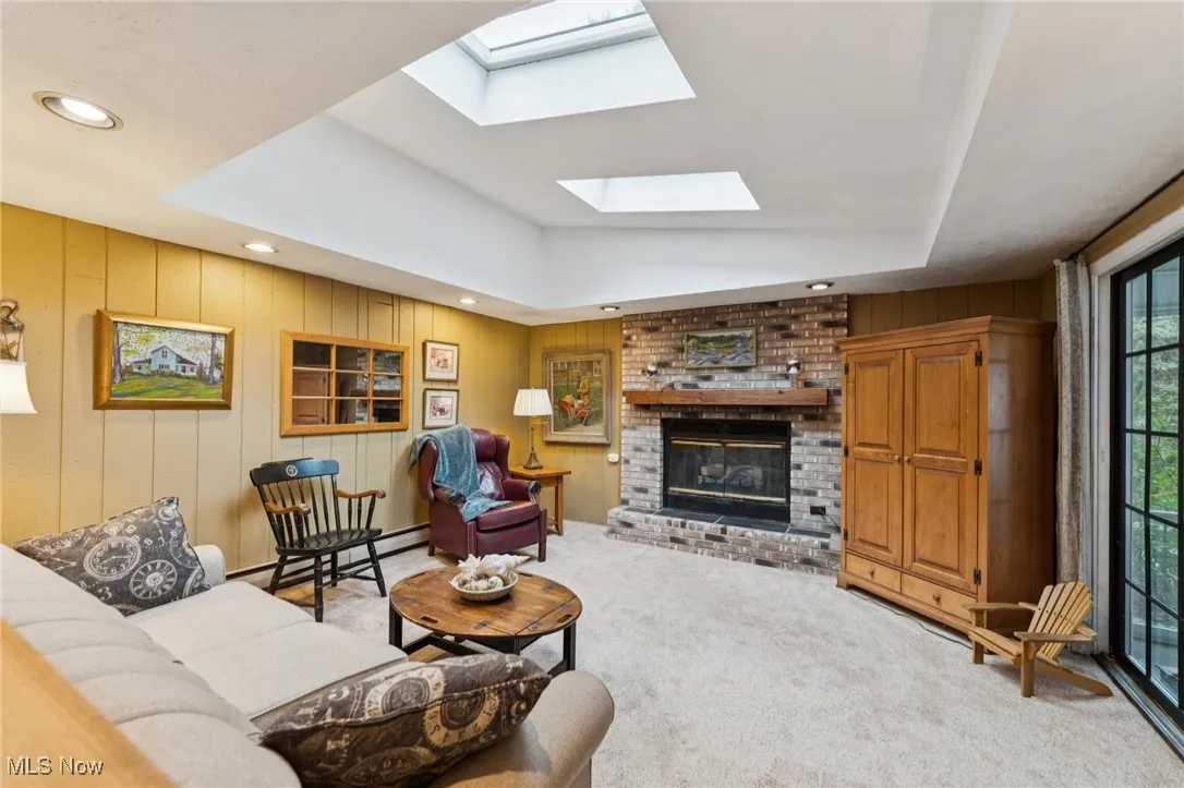 Carpeted living room featuring wooden walls, a fireplace, baseboard heating, a raised ceiling, and recessed lighting