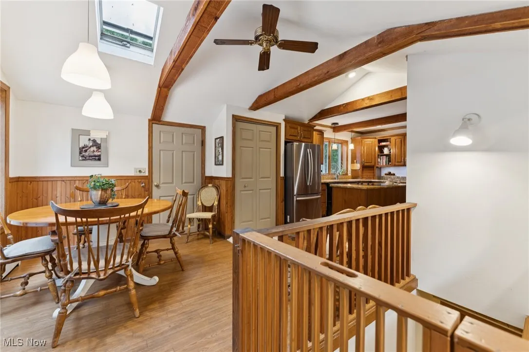 Dining space featuring light wood finished floors, ceiling fan, a skylight, and a wainscoted wall