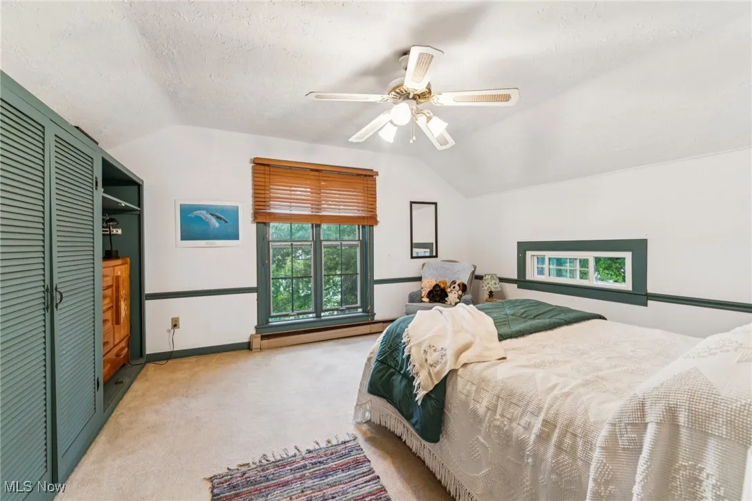 Carpeted bedroom featuring lofted ceiling, a closet, a textured ceiling, a ceiling fan, and baseboard heating
