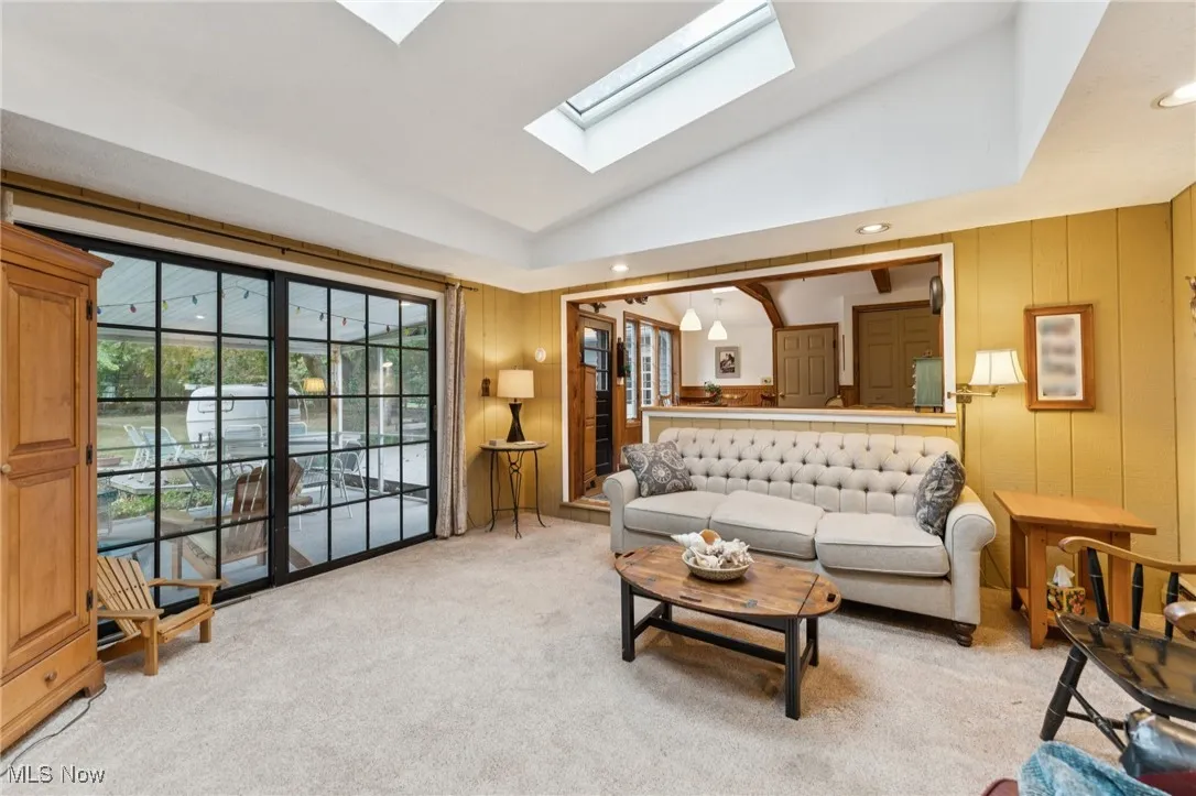 Living room featuring lofted ceiling, light carpet, wood walls, a skylight, and recessed lighting