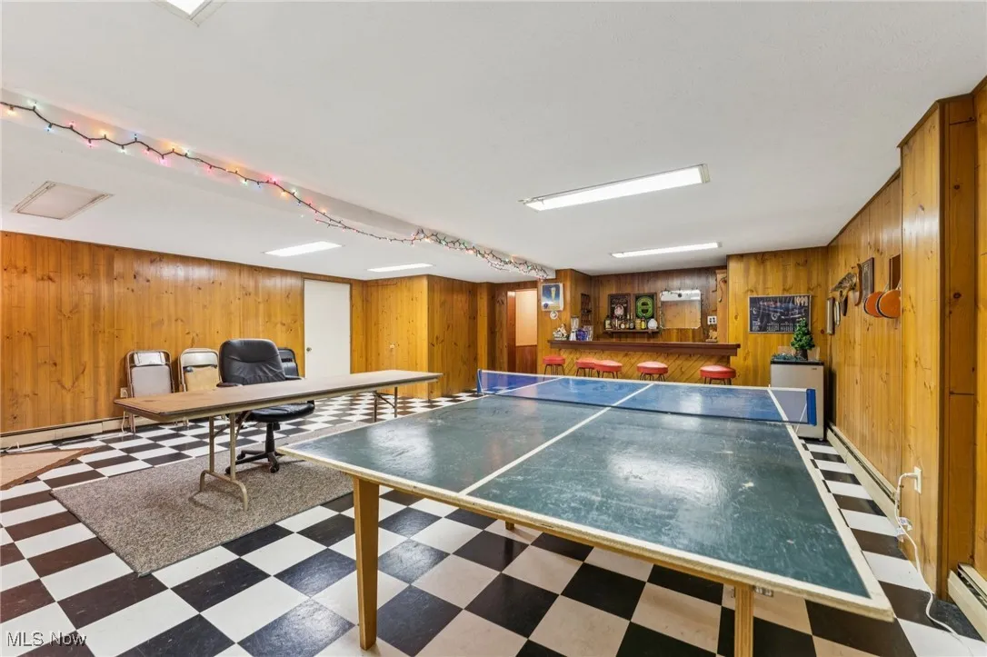Recreation room with tile patterned floors, a baseboard heating unit, and wood walls