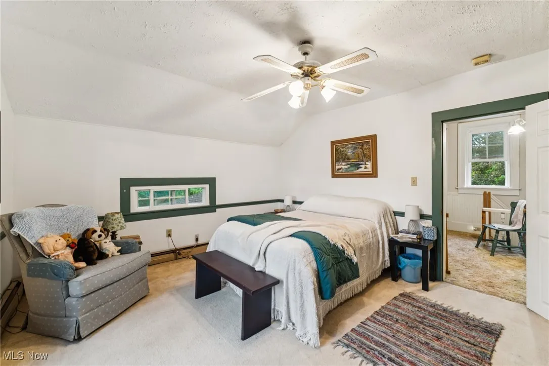 Bedroom with a textured ceiling, baseboard heating, ceiling fan, lofted ceiling, and carpet