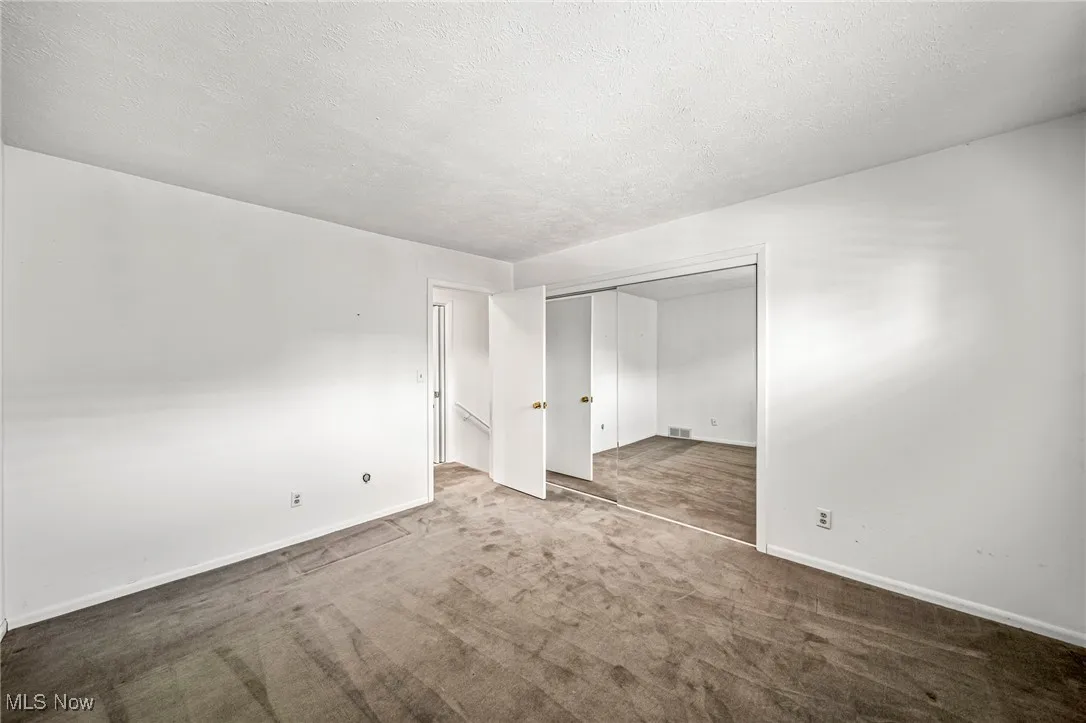 Unfurnished bedroom featuring dark carpet, a textured ceiling, and a closet