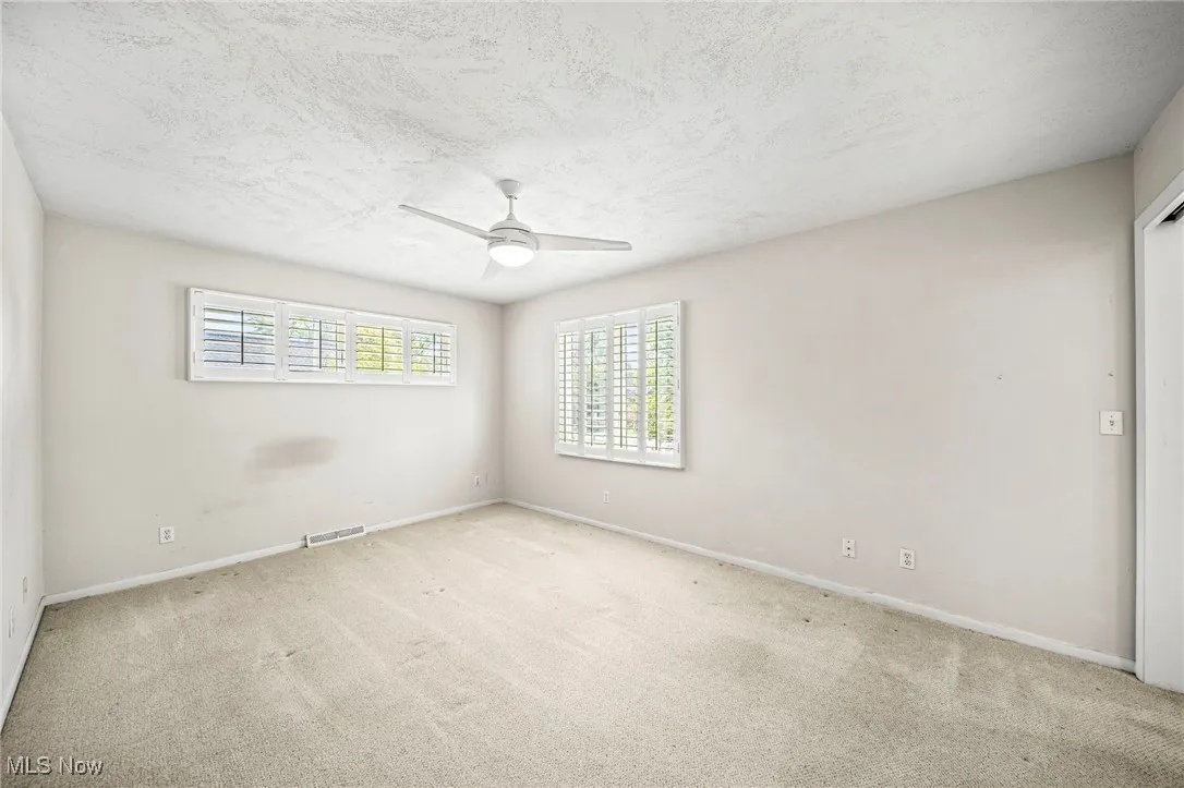 Empty room featuring carpet flooring, a textured ceiling, and ceiling fan