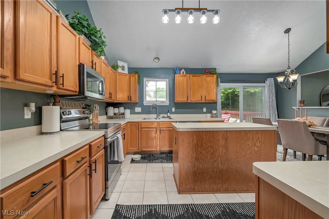 Kitchen with appliances with stainless steel finishes, brown cabinets, light countertops, pendant lighting, and light tile patterned flooring