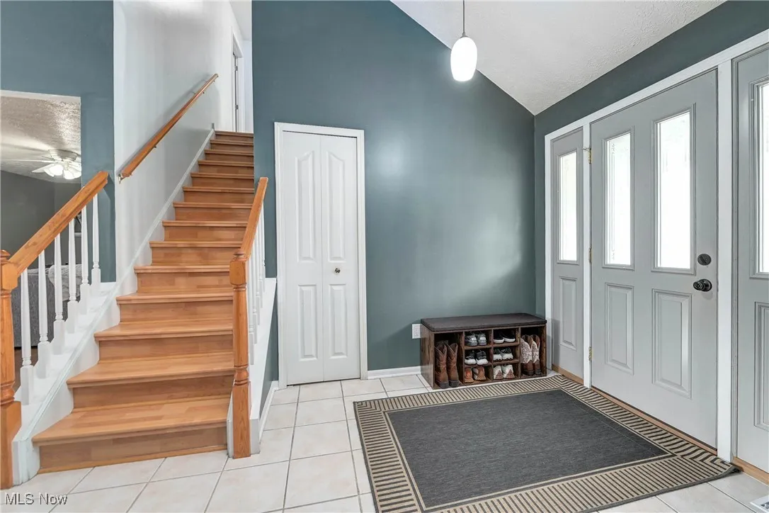 Entryway with light tile patterned flooring, stairs, and lofted ceiling