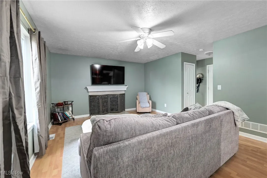 Living area with a textured ceiling, a ceiling fan, and light wood-type flooring