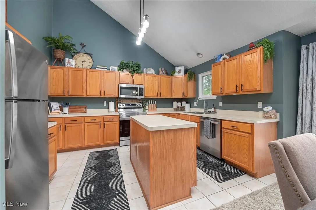 Kitchen with stainless steel appliances, light countertops, light tile patterned floors, and high vaulted ceiling