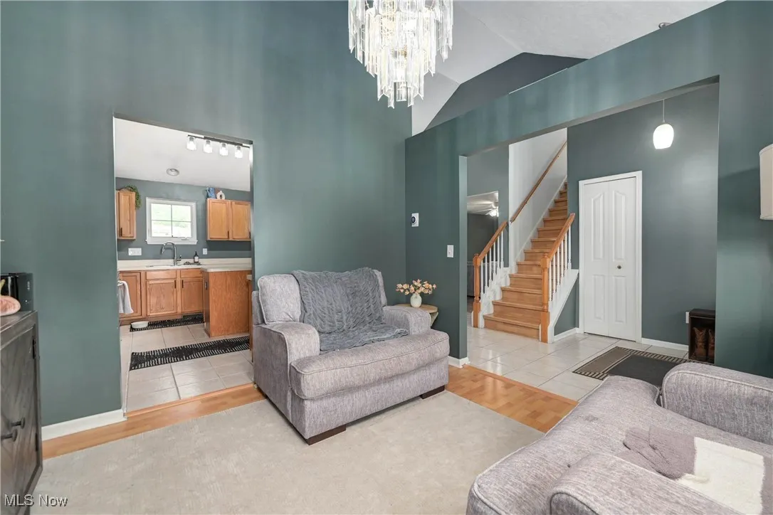 Living room with light tile patterned floors, high vaulted ceiling, stairway, and a chandelier