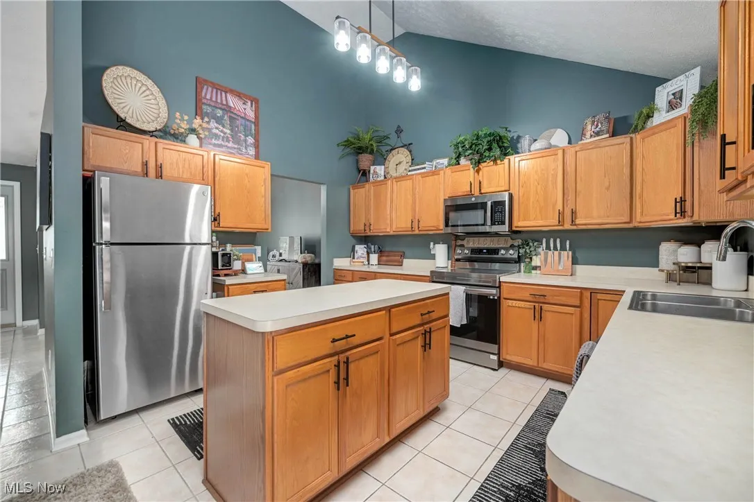 Kitchen with light countertops, appliances with stainless steel finishes, high vaulted ceiling, light tile patterned floors, and decorative light fixtures