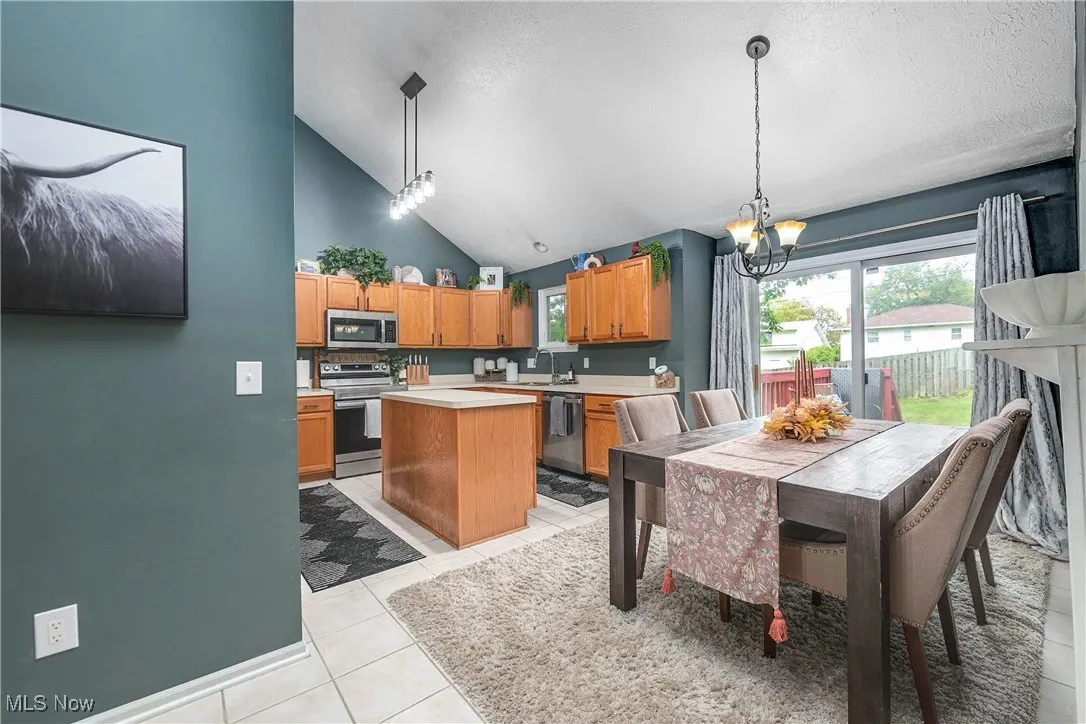 Kitchen featuring brown cabinetry, light countertops, decorative light fixtures, light tile patterned floors, and high vaulted ceiling