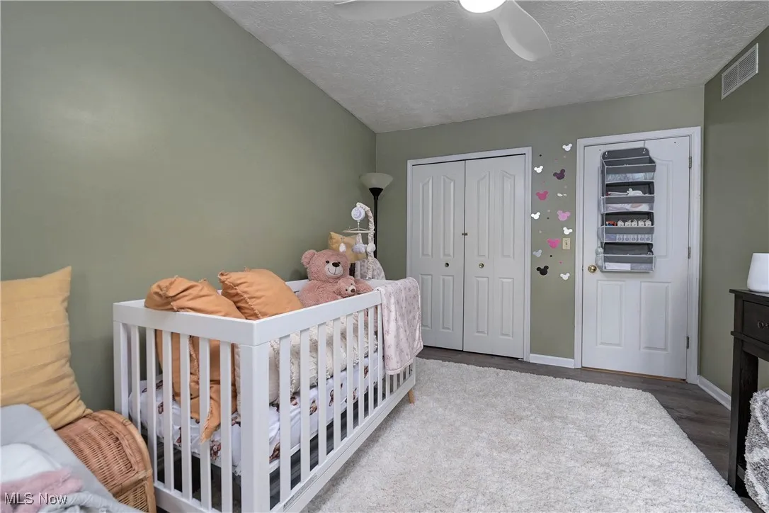 Bedroom featuring wood finished floors, a closet, a textured ceiling, a nursery area, and ceiling fan