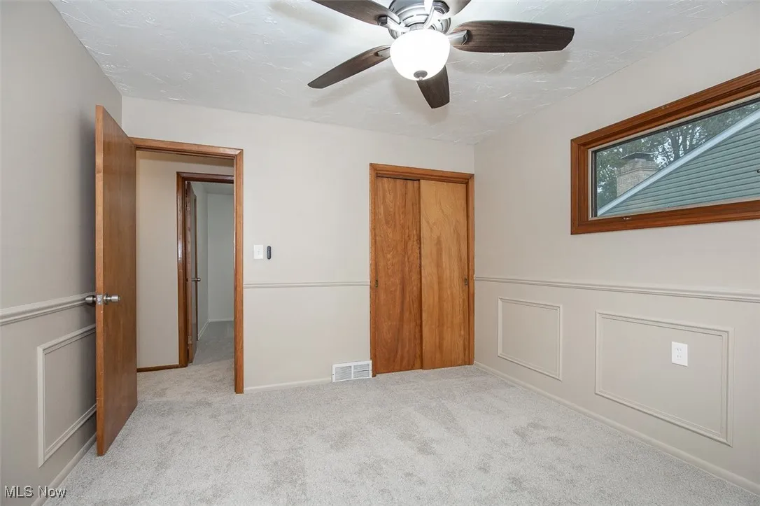 Unfurnished bedroom featuring light colored carpet, ceiling fan, a closet, and a decorative wall