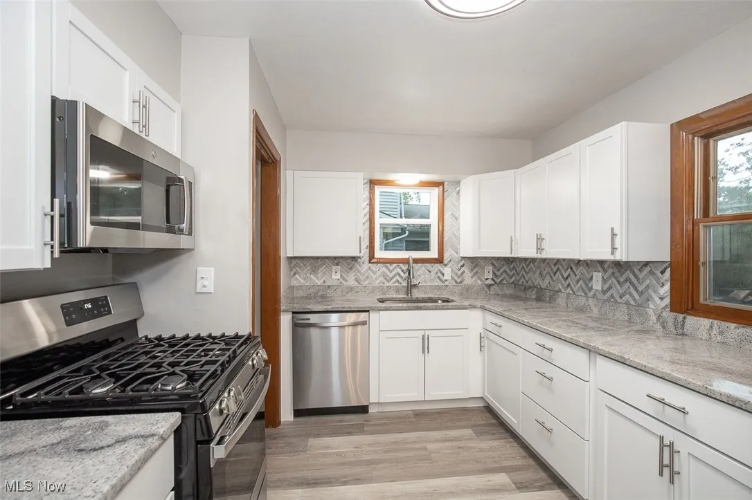 Kitchen with stainless steel appliances, light stone countertops, white cabinetry, and light wood-style flooring