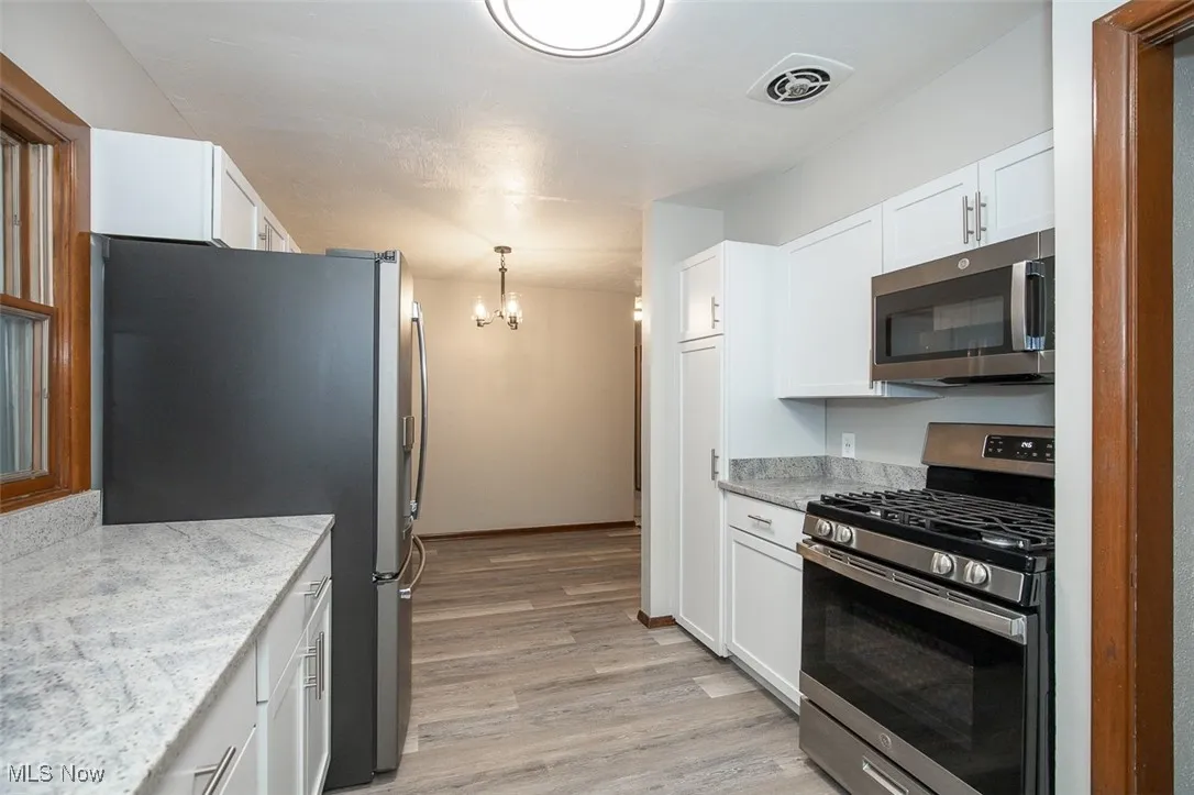 Kitchen with stainless steel appliances, white cabinets, a chandelier, pendant lighting, and light stone countertops
