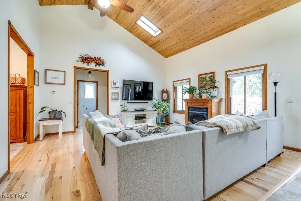 Living area with high vaulted ceiling, a glass covered fireplace, plenty of natural light, light wood-style flooring, and a wood ceiling with exposed beams