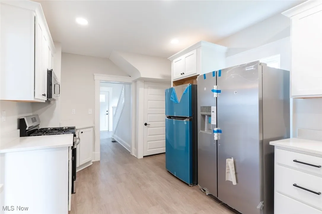 Kitchen with white cabinets, appliances with stainless steel finishes, light wood finished floors, light stone counters, and recessed lighting
