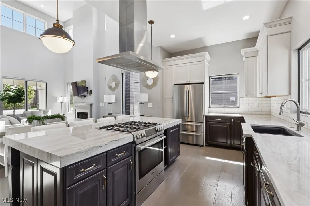 Kitchen with appliances with stainless steel finishes, island range hood, light stone countertops, open floor plan, and hanging light fixtures