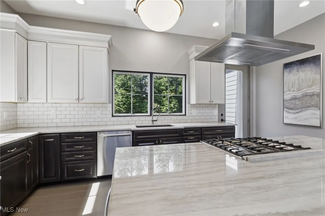 Kitchen with white cabinetry, island range hood, light stone countertops, appliances with stainless steel finishes, and recessed lighting