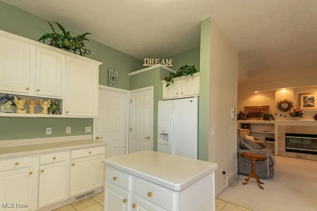 Kitchen with white refrigerator with ice dispenser, white cabinets, light countertops, open shelves, and a kitchen island
