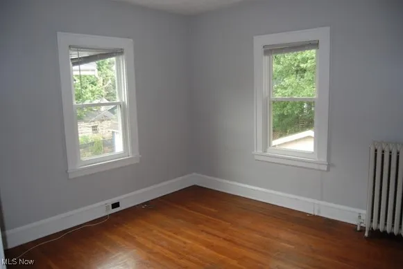 Empty room with radiator heating unit and dark wood-type flooring