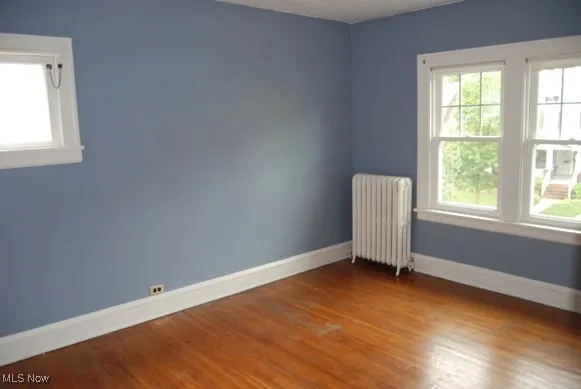 Unfurnished room with radiator heating unit and wood finished floors
